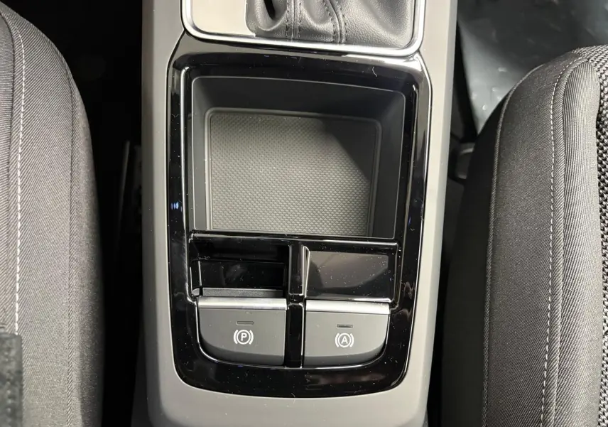 Gros plan sur la console centrale noire brillante entre les sièges avant en tissu gris de l'Audi Q2 35 TFSI S Line.