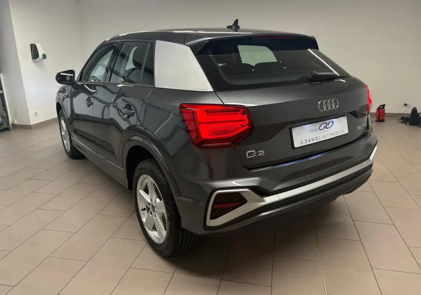 Audi Q2 35 TFSI S Line gris Daytona en 3/4 arrière droit, avec toit noir et montant arrière argenté contrastant.
