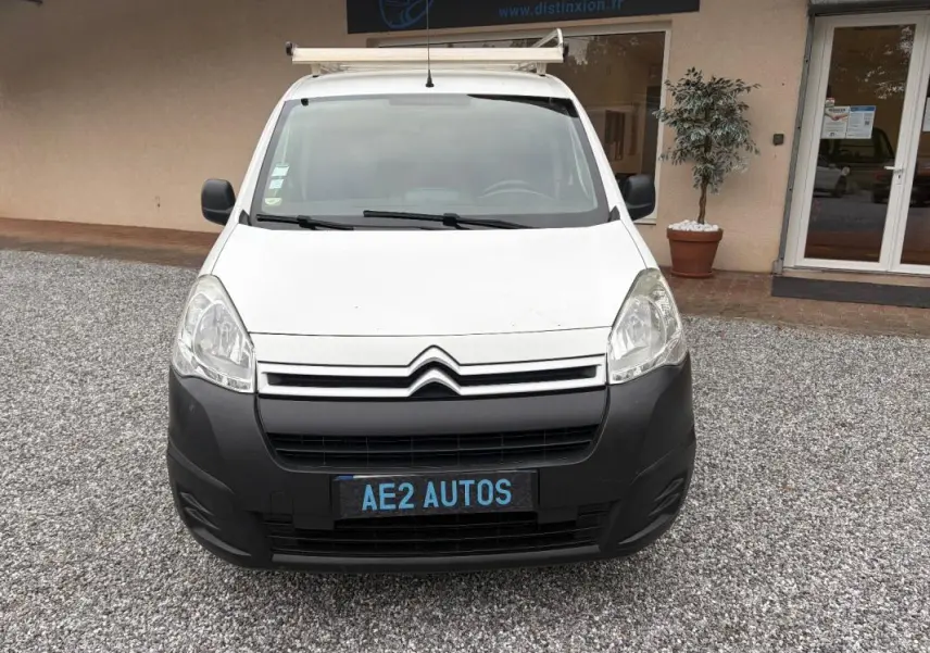 Vue de face d’un Citroën Berlingo blanc 2018 avec pare-chocs noir et galerie de toit, stationné sur gravier.