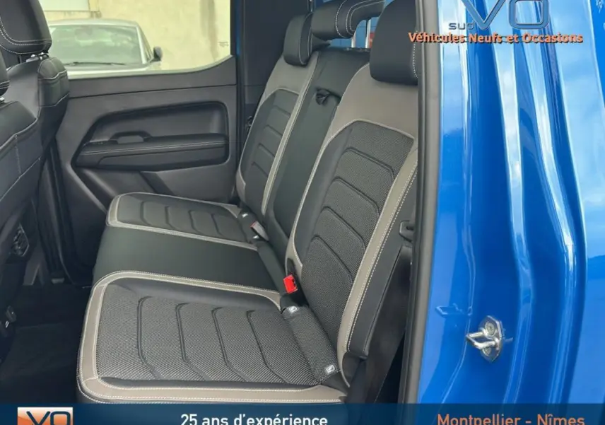 Vue latérale des sièges arrière en cuir noir et gris du Volkswagen Amarok Simple Cabine bleu 2025, avec porte ouverte.