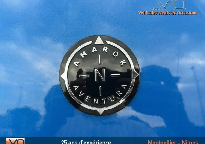 Gros plan sur l'écusson noir et chrome Amarok Aventura sur la carrosserie bleu vif du Volkswagen Amarok 2025.