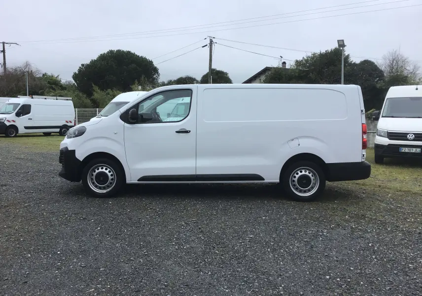 Vue de profil côté gauche d’un FIAT Scudo Fourgon blanc 2024 avec garde au sol réhaussée et protections noires visibles.