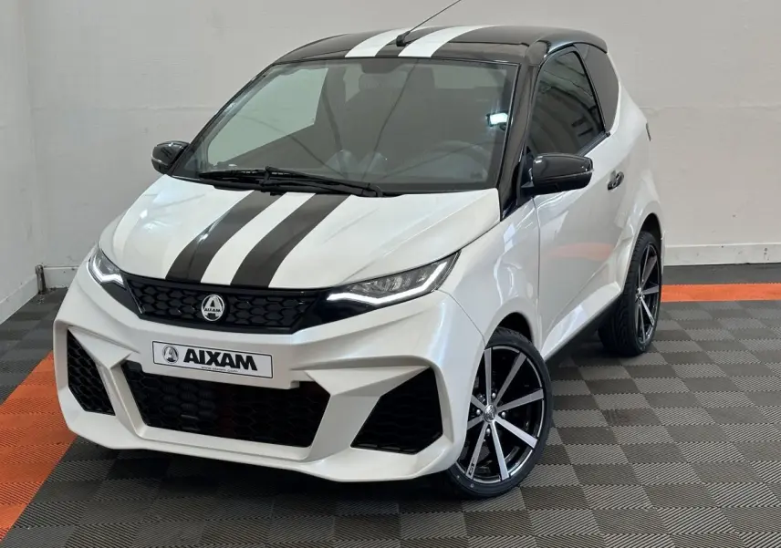 Vue 3/4 avant droite d'une Aixam Ambition 0.5 City GTO blanche avec bandes noires et jantes noires à rayures argentées.