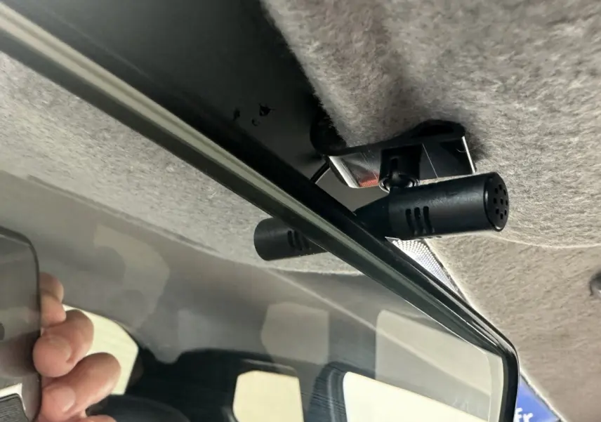 Gros plan intérieur sur la caméra fixée au plafond, au-dessus du rétroviseur d'une Aixam Ambition blanche.