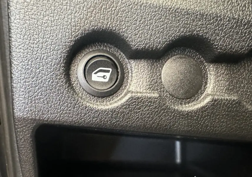 Gros plan sur un bouton de commande de coffre dans l’habitacle noir texturé de l’AIXAM AMBITION 0.5 CITY GTO blanc.