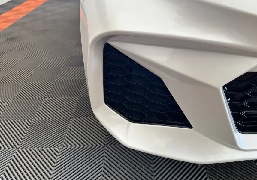 Gros plan sur l'entrée d'air avant gauche d'une Aixam Ambition 0.5 City GTO blanche, soulignant sa calandre noire hexagonale.