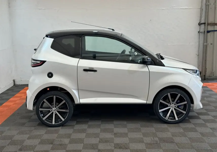 Vue de profil côté gauche d'une Aixam Ambition 0.5 City GTO blanche avec toit noir et jantes noires en intérieur.