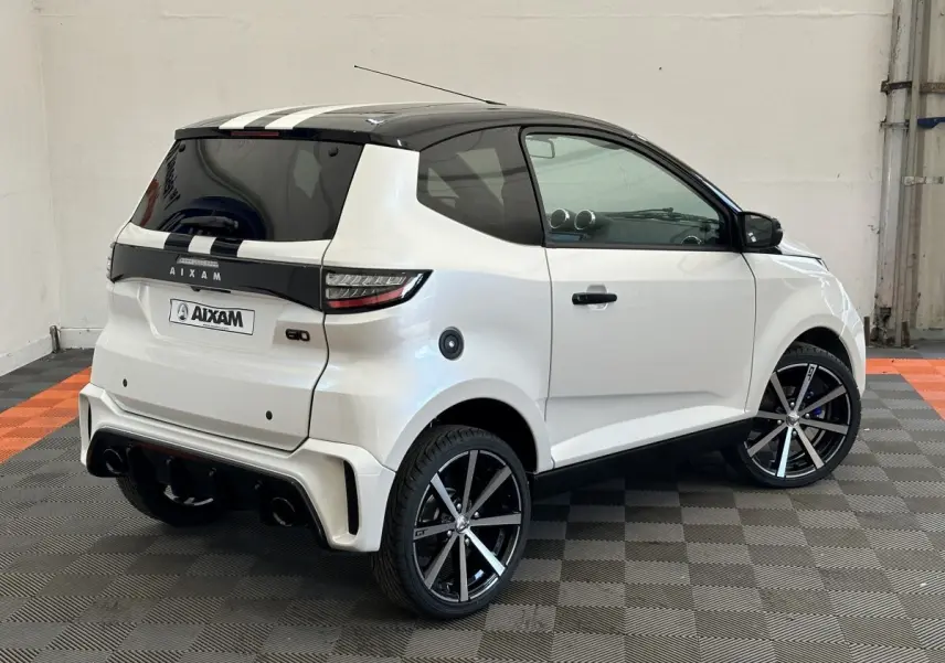 Vue 3/4 arrière droite de l'AIXAM AMBITION 0.5 CITY GTO blanche avec toit noir et jantes noires à rayures argentées.