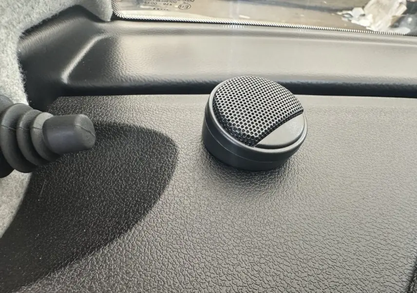 Gros plan sur un haut-parleur noir intégré au tableau de bord texturé d’une Aixam Ambition 0.5 City GTO blanche.