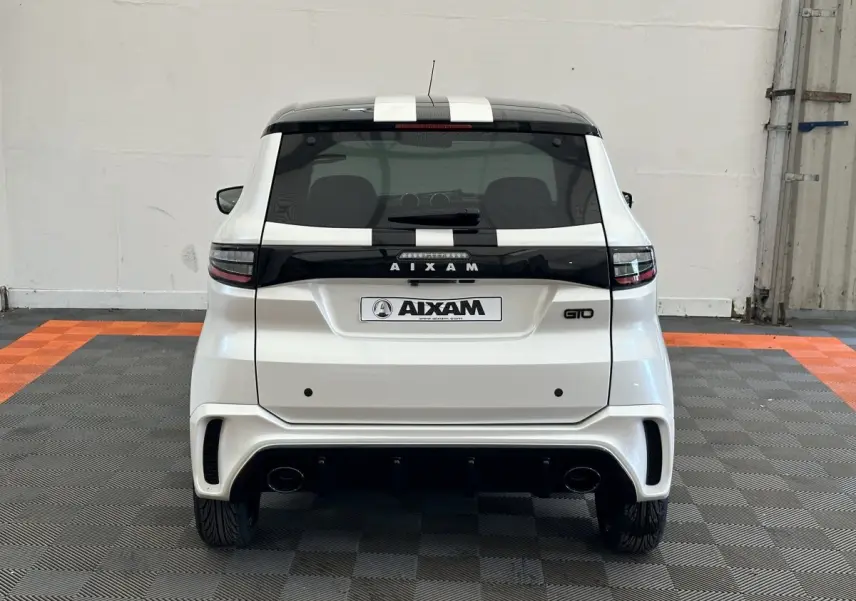 Vue arrière d'une Aixam Ambition 0.5 City GTO blanche avec toit noir et bandes noires, en intérieur sur sol carrelé.