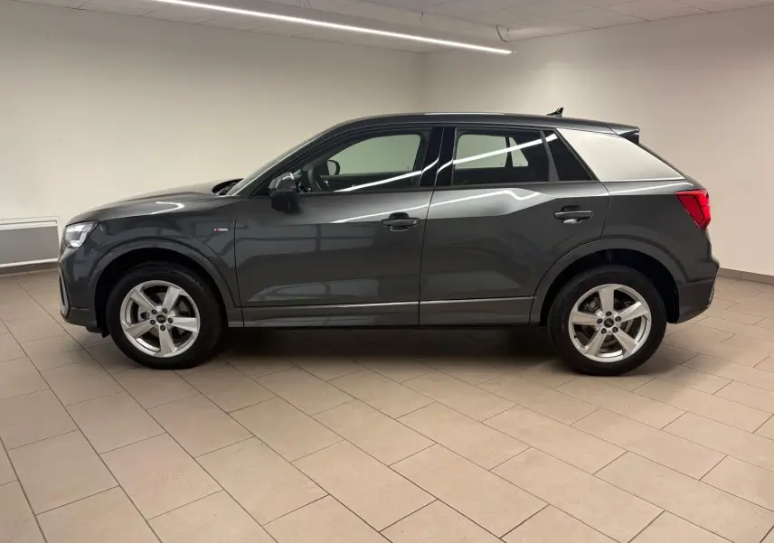 Vue de profil côté gauche d'un Audi Q2 35 TFSI S Line gris Daytona métallisé dans un intérieur neutre.