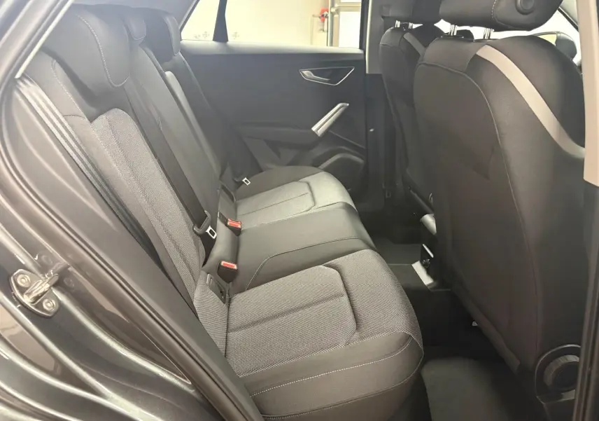 Vue intérieure côté gauche des sièges arrière gris foncé de l'Audi Q2 35 TFSI S Line 2026 avec porte ouverte.