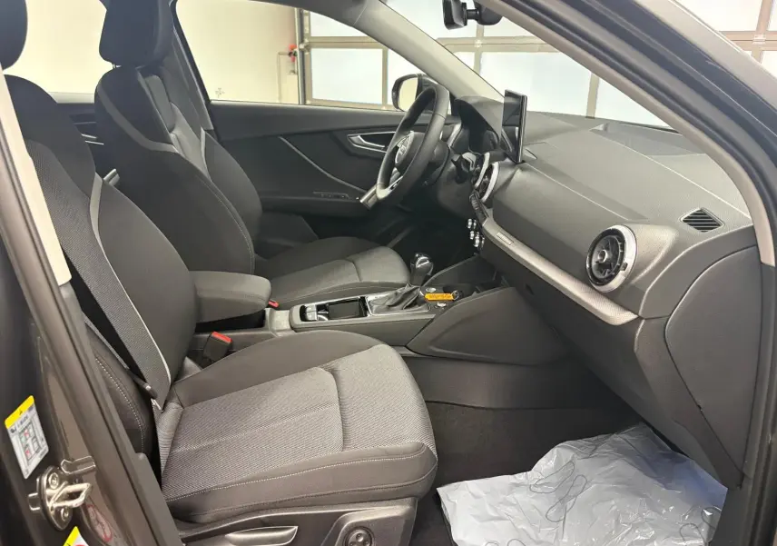 Vue intérieure côté conducteur de l'Audi Q2 35 TFSI S Line 2026 avec sièges tissu gris et tableau de bord moderne.