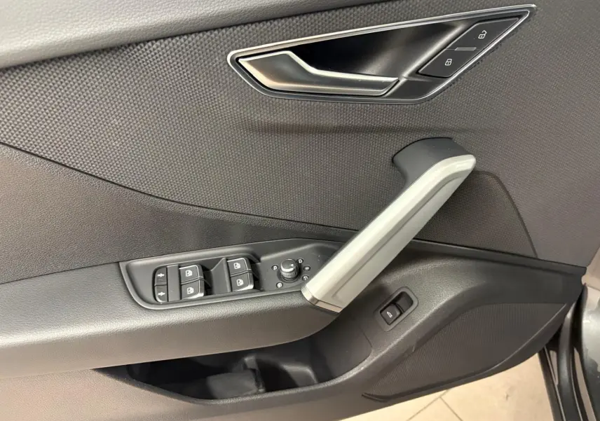 Gros plan sur la porte côté conducteur de l'Audi Q2 35 TFSI S Line 2026 en Gris Daytona, avec commandes de vitres et poignée argentée.