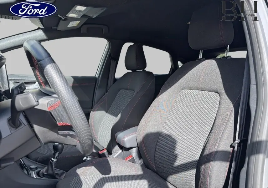 Vue intérieure côté conducteur du Ford Puma 2024, sièges tissu noir avec surpiqûres rouges et volant cuir perforé.