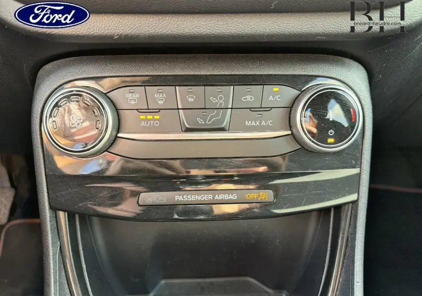 Gros plan sur la console centrale du Ford Puma 2024 gris Solar, montrant les commandes de climatisation et l'indicateur airbag passager.