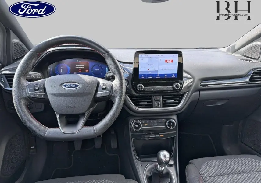 Vue intérieure frontale du tableau de bord du Ford Puma 2024 avec volant multifonction, écran tactile central et levier de vitesses manuel.