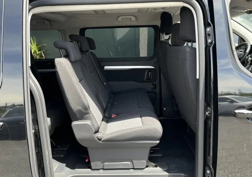 Vue latérale intérieure du Citroën Spacetourer XL noir Perla, montrant les sièges passagers en tissu gris et portes latérales ouvertes.
