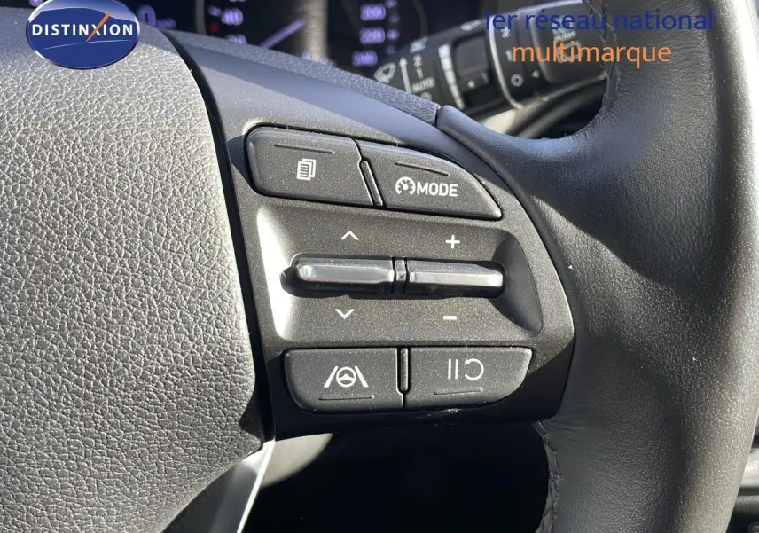Gros plan sur les commandes au volant à droite d'une Hyundai i30 SW 2024 couleur Dark Knight Metal, avec boutons mode et régulateur.