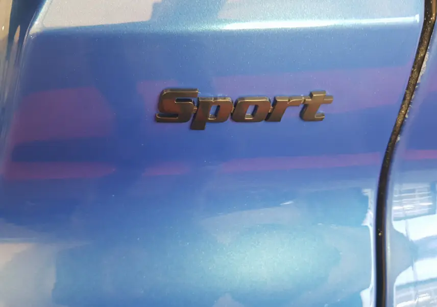 Gros plan sur l’inscription Sport en noir sur la carrosserie bleu métallisé de l’AIXAM AMBITION 0.5 CITY SPORT.