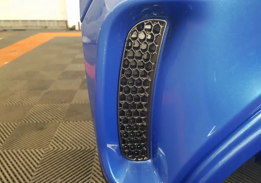 Gros plan sur la prise d'air noire en nid d'abeille du côté gauche de l'AIXAM AMBITION 0.5 CITY SPORT bleu.