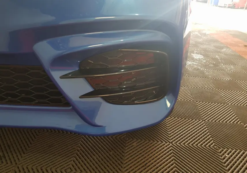 Gros plan sur la partie avant droite bleue de l'AIXAM AMBITION 0.5 CITY SPORT avec grille noire et détails aérés.