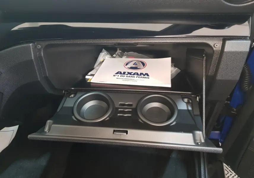 Gros plan sur la boîte à gants ouverte de l'AIXAM Ambition 0.5 City Sport bleu, avec porte-gobelets et manuel utilisateur visible.