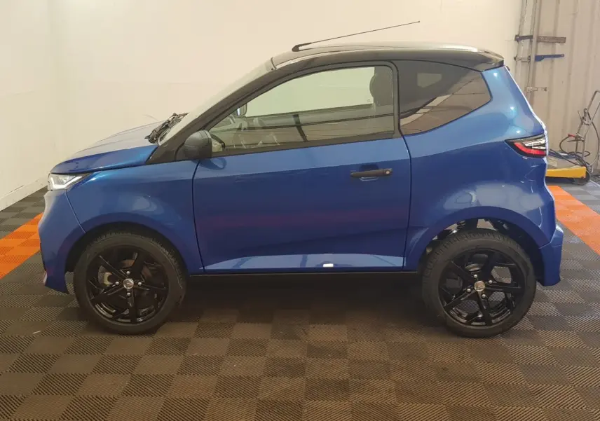 Vue de profil côté gauche d'une Aixam Ambition 0.5 City Sport bleu 2026 avec jantes noires et rétroviseur caméra.