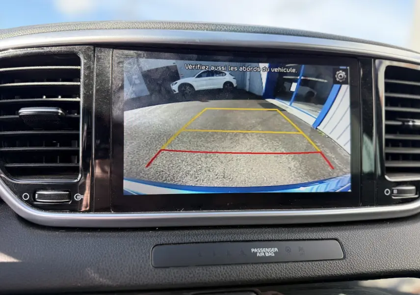Écran central montrant la caméra de recul du Kia Sportage bleu, avec lignes de guidage en rouge et jaune.
