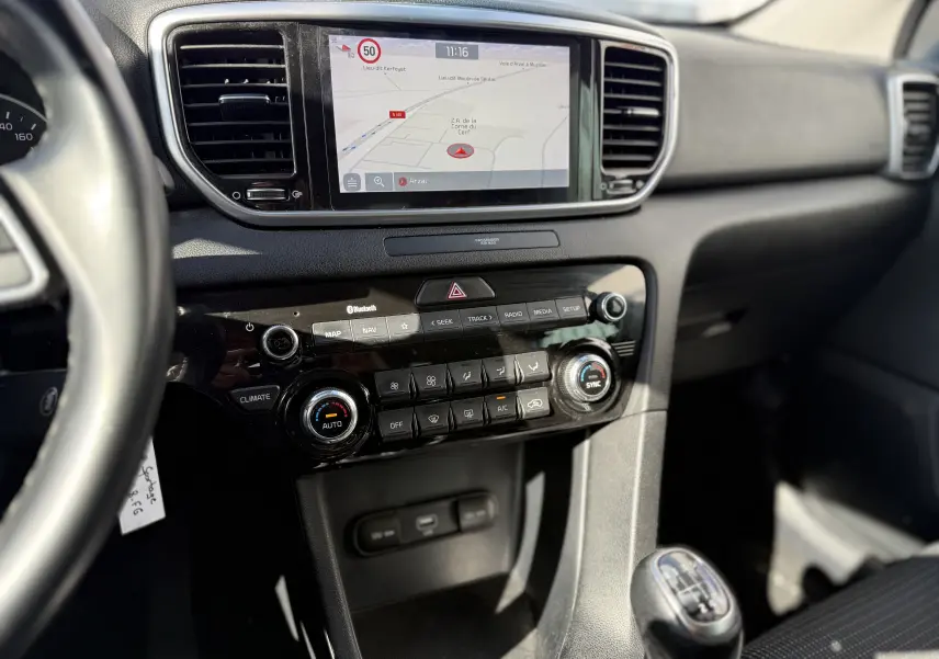 Vue intérieure centrée sur la console centrale du Kia Sportage bleu 2021, avec écran tactile et levier de vitesse manuel.
