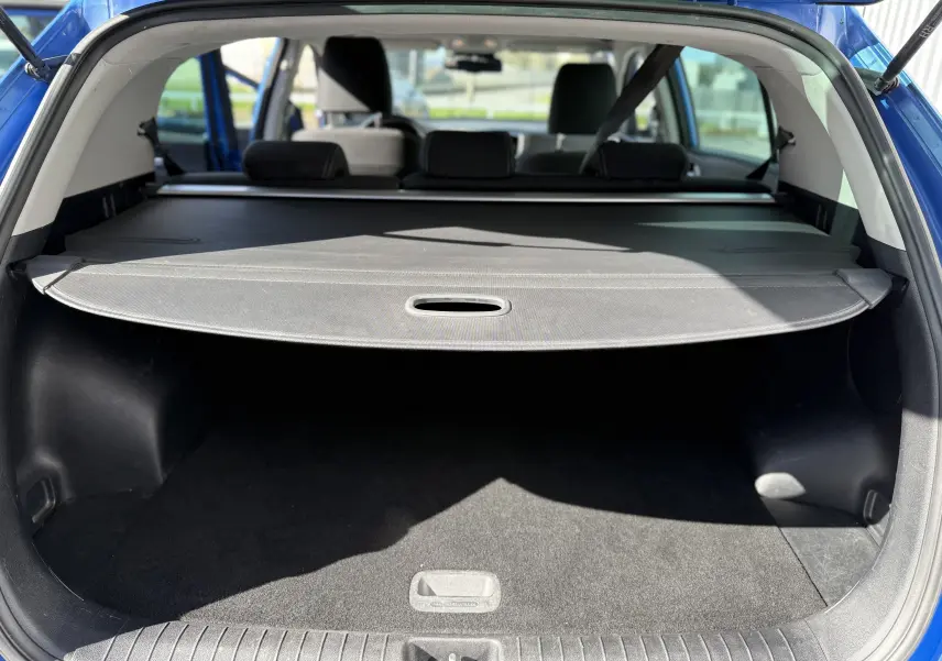 Coffre ouvert vu de l'arrière d'un Kia Sportage bleu 2021, avec cache-bagages déployé et intérieur noir.