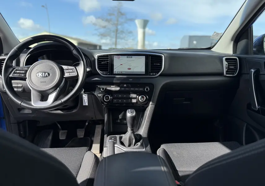 Vue intérieure avant du Kia Sportage 1.6 CRDI 136 Black Edition 2021 bleu, avec tableau de bord et boîte manuelle visibles.