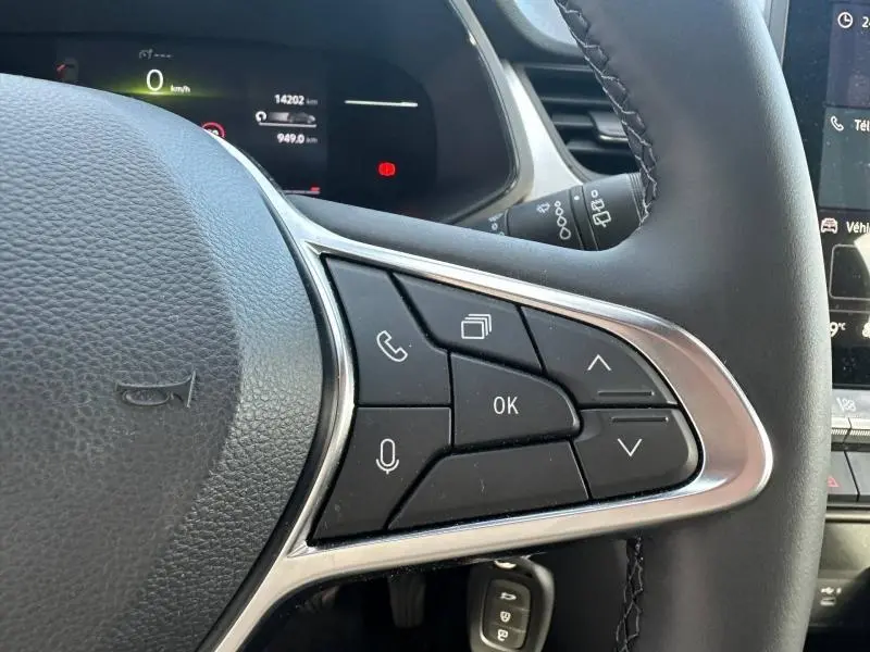 Gros plan sur les commandes multifonctions à droite du volant noir du Renault Captur blanc nacré 2025, avec écran digital en arrière-plan.