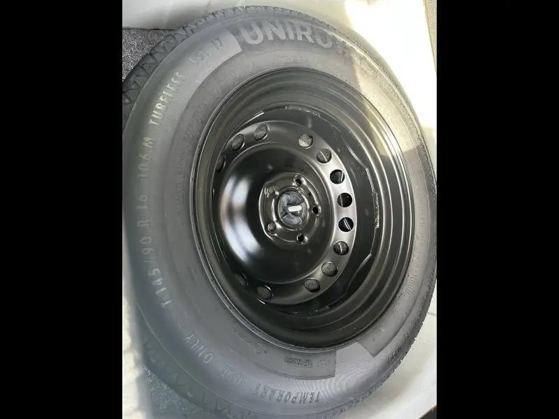 Gros plan sur la roue de secours noire en acier du Renault Captur blanc nacré/ noir étoile, visible dans le coffre.
