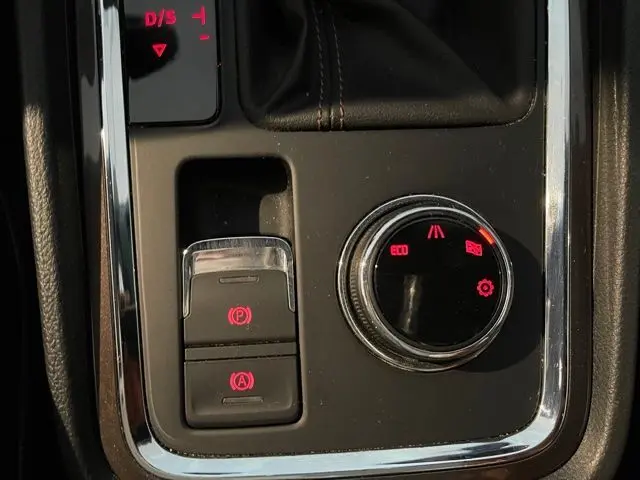 Gros plan sur la console centrale noire du SEAT Ateca avec commandes électroniques et bouton de mode de conduite éclairés en rouge.
