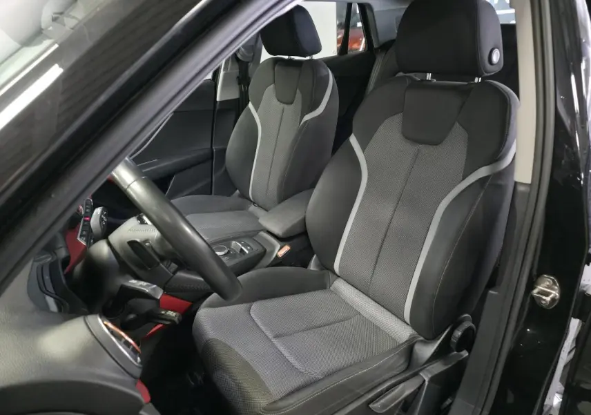 Vue intérieure côté conducteur de l'Audi Q2 noir avec sièges sport en tissu gris et applications décoratives rouges.