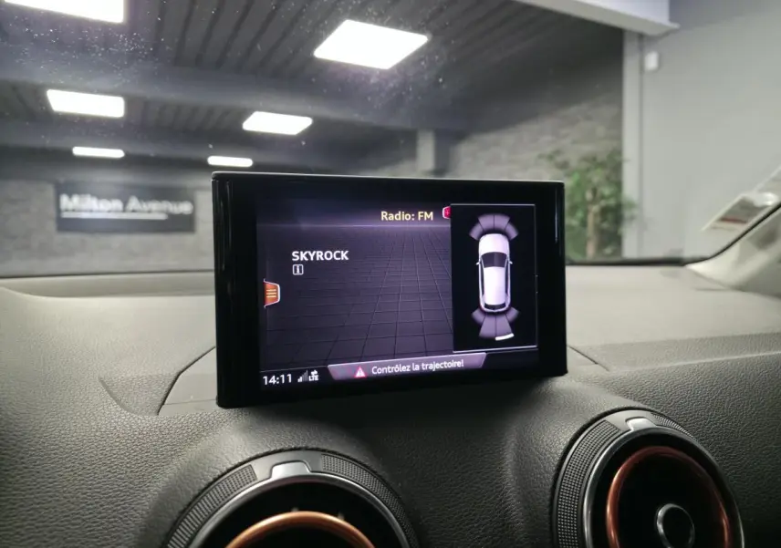 Écran MMI central affichant la radio FM et l'aide au stationnement dans l'Audi Q2 noire, vue intérieure avant.