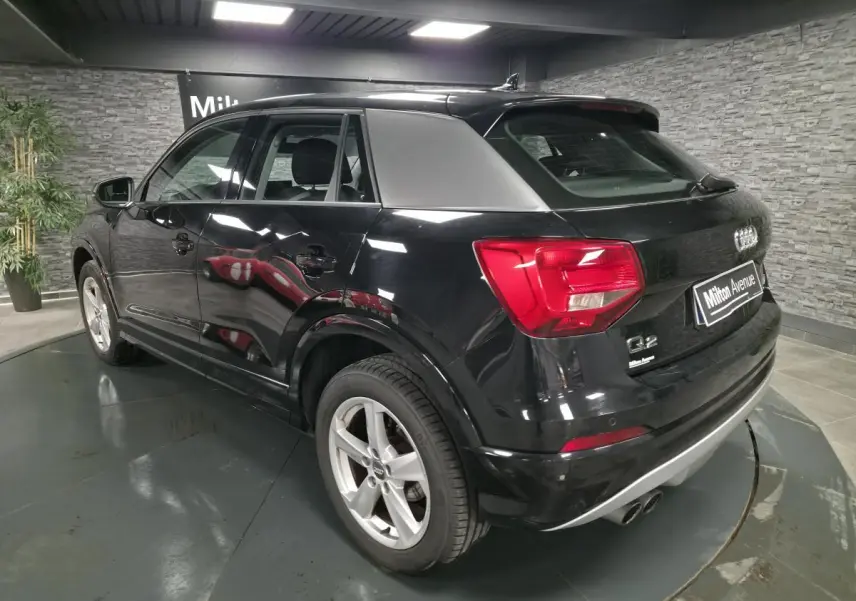 Audi Q2 noir en 3/4 arrière droit, avec jantes 5 branches et feux arrière rouges dans un showroom.
