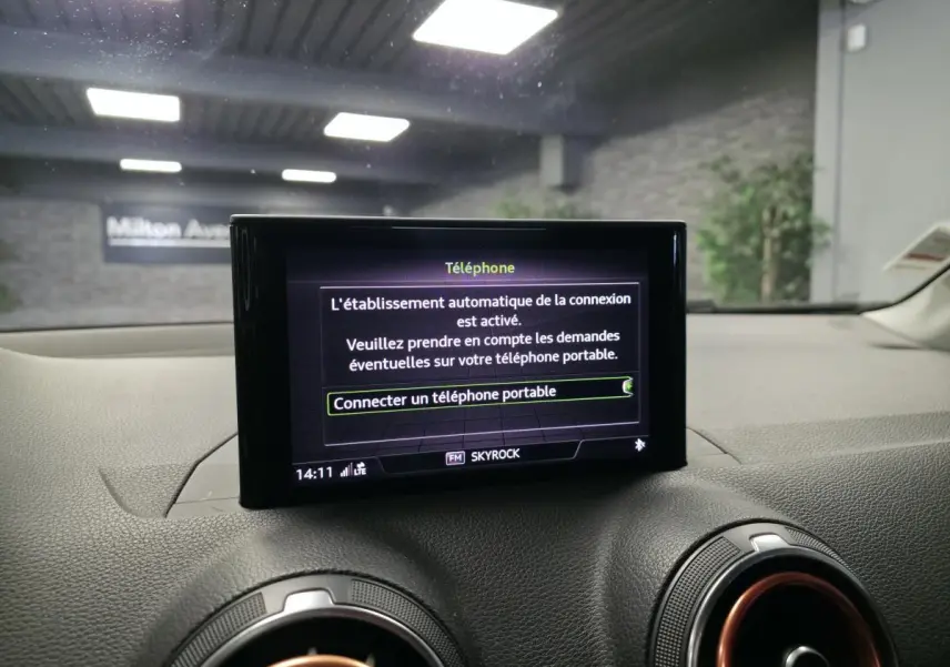 Écran MMI central affichant la connexion téléphone dans l'Audi Q2 1.4 TFSI noir, intérieur avec aérateurs cerclés rouges.