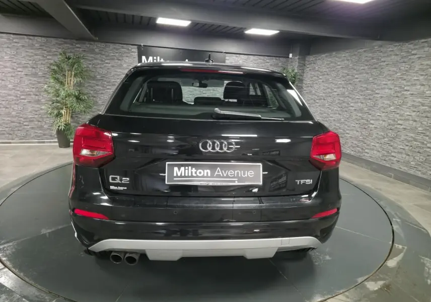 Vue arrière d'un Audi Q2 noir avec double sortie d'échappement à gauche et logo TFSI sur un plateau tournant intérieur.