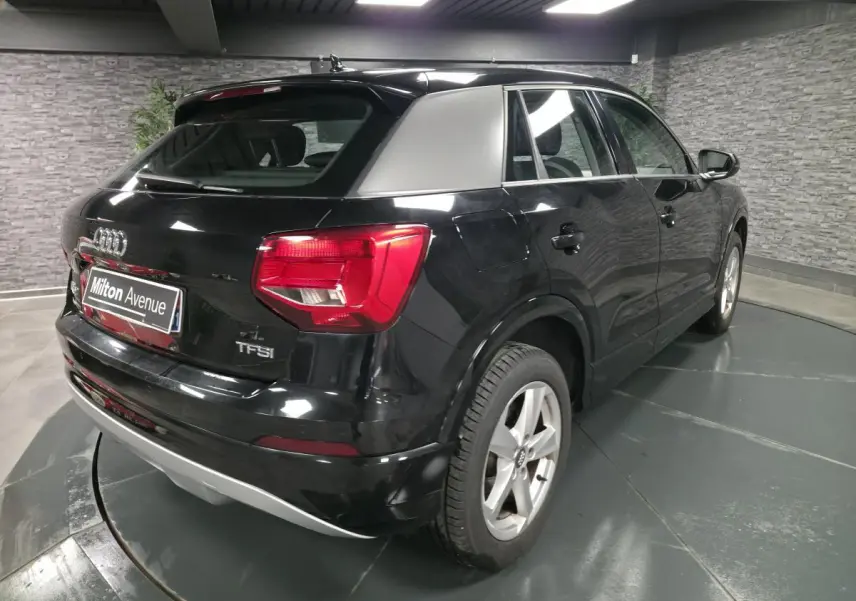 Audi Q2 noir vue 3/4 arrière droit avec toit argenté et feux arrière rouges en intérieur showroom.