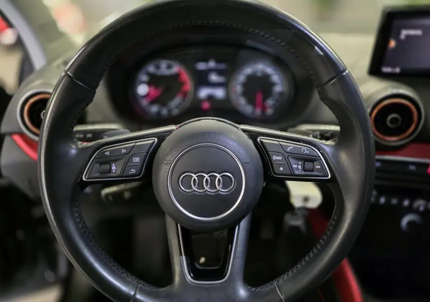 Volant cuir noir multifonction Audi Q2 1.4 TFSI Sport avec tableau de bord et applications décoratives rouges visibles en arrière-plan