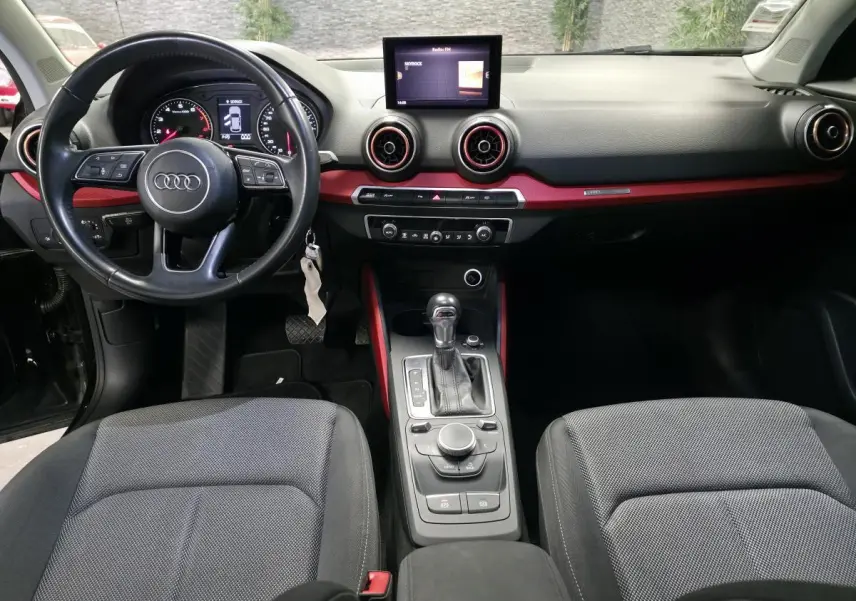 Intérieur Audi Q2 2017 noir, vue avant centrée sur tableau de bord avec applications rouges et console centrale automatique.