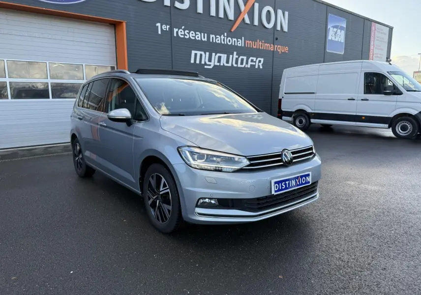 Volkswagen Touran argent Dolomite en 3/4 avant droit, avec jantes alliage et toit ouvrant panoramique visible.
