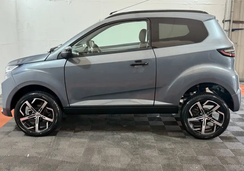 Vue de profil côté gauche d'une Aixam Ambition 0.5 Crossover Premium gris foncé avec rétroviseur caméra côté conducteur.