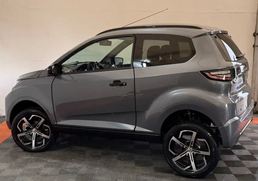 Vue de profil côté gauche d'une Aixam Ambition 0.5 Crossover Premium gris foncé avec jantes alliage et rétroviseur caméra.