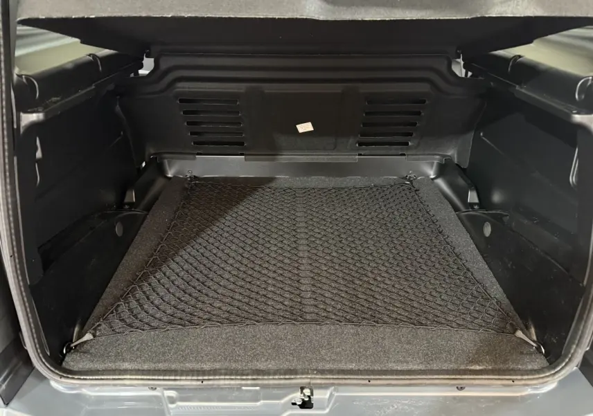 Coffre ouvert vu de l'arrière d'une Aixam Ambition 0.5 Crossover Premium gris foncé, avec filet de rangement au sol.