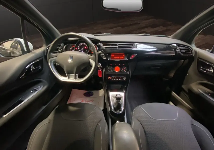 Vue intérieure avant de la Citroën DS3 1.6 e-HDI 90 AirDream So Chic, tableau de bord noir avec volant et console centrale.