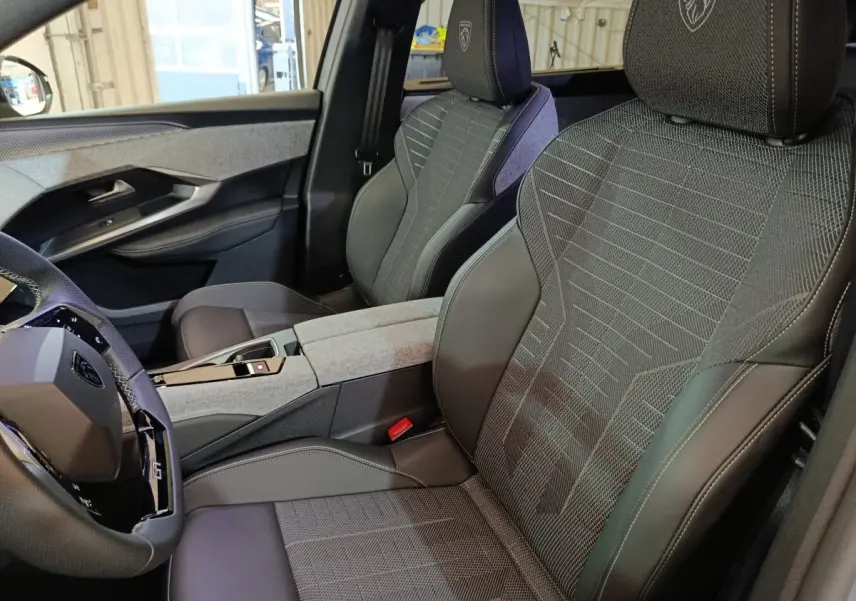 Vue intérieure côté conducteur du Peugeot 5008 GT 2026, sièges tissu et cuir gris avec logo lion brodé sur appuie-tête.