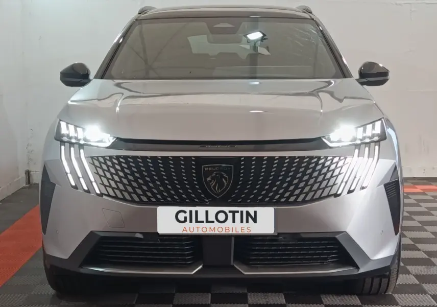 Vue frontale d'un Peugeot 5008 gris clair 2026 avec phares LED allumés et calandre distinctive au lion.